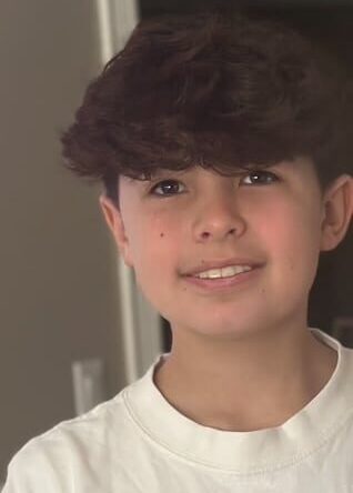 This image is the owner son. He is 14. He has wavy/curly brown hair, brown eyes and a beautiful smile. He's wearing a white T-shirt and he is standing in front of a gray wall. It's just the basic picture a very close-up of his face.